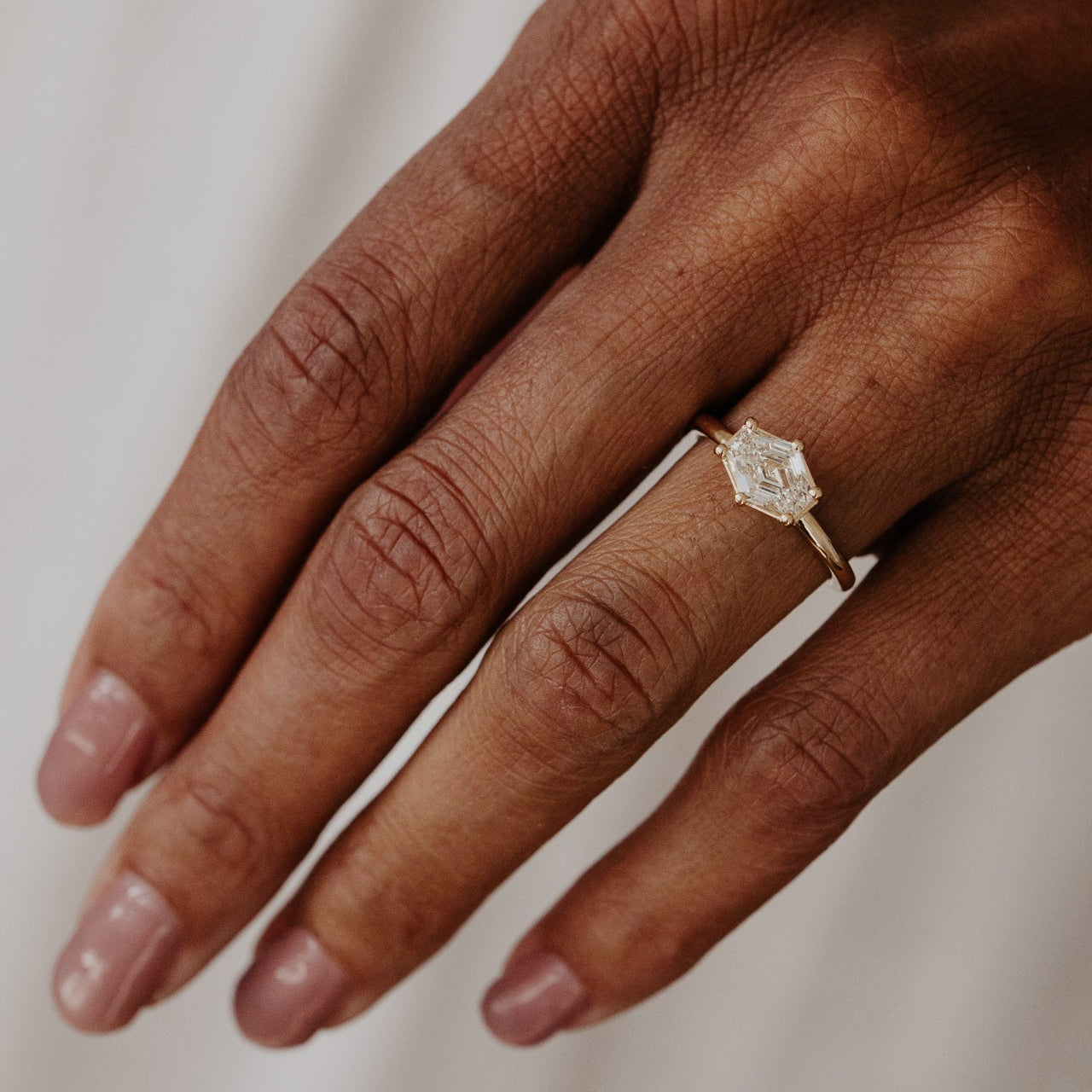 Hand wearing a champagne diamond ring on a neutral background.