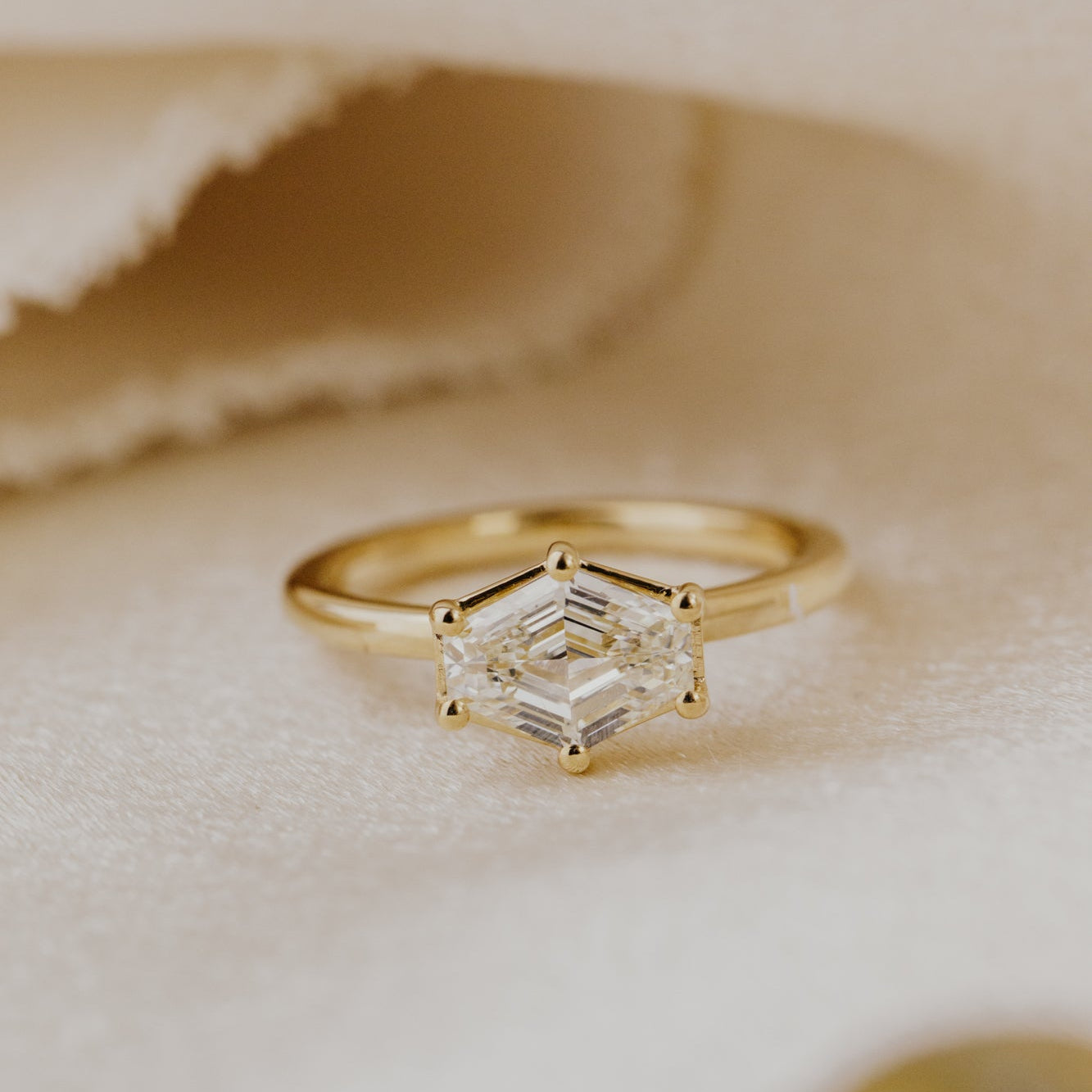 Gold ring with a champagne diamond on a soft beige fabric background.