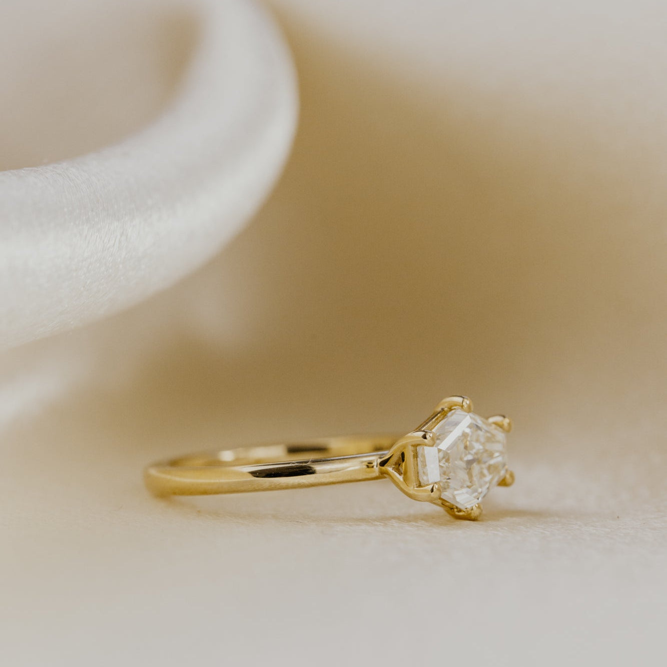 Gold ring with a diamond on a soft beige background.
