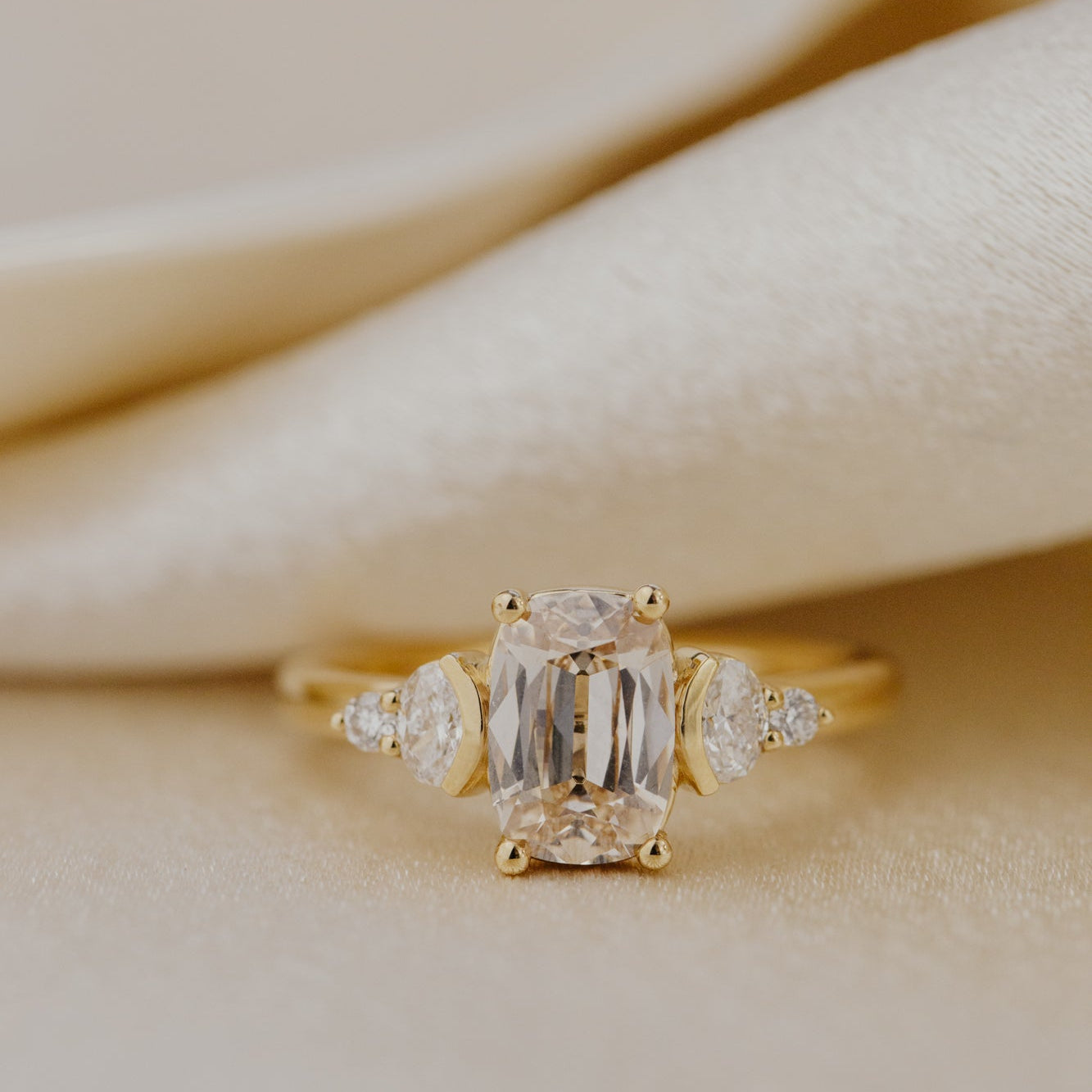Gold ring with a central champagne diamond and smaller side stones on a beige fabric background.