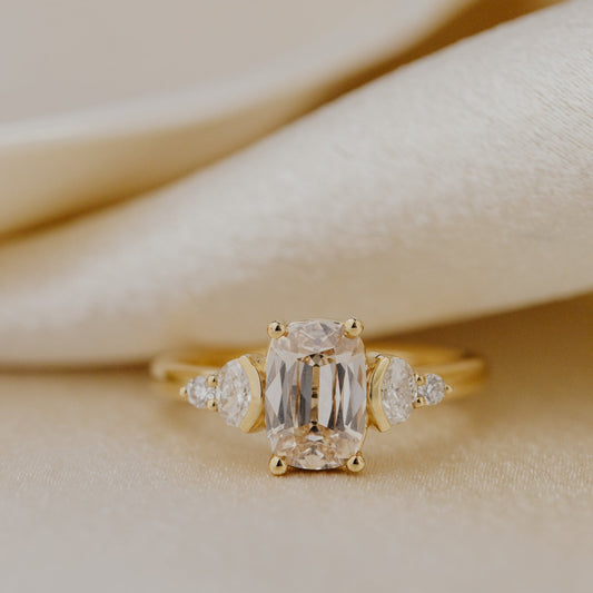 Gold ring with a central champagne diamond and smaller side stones on a beige fabric background.