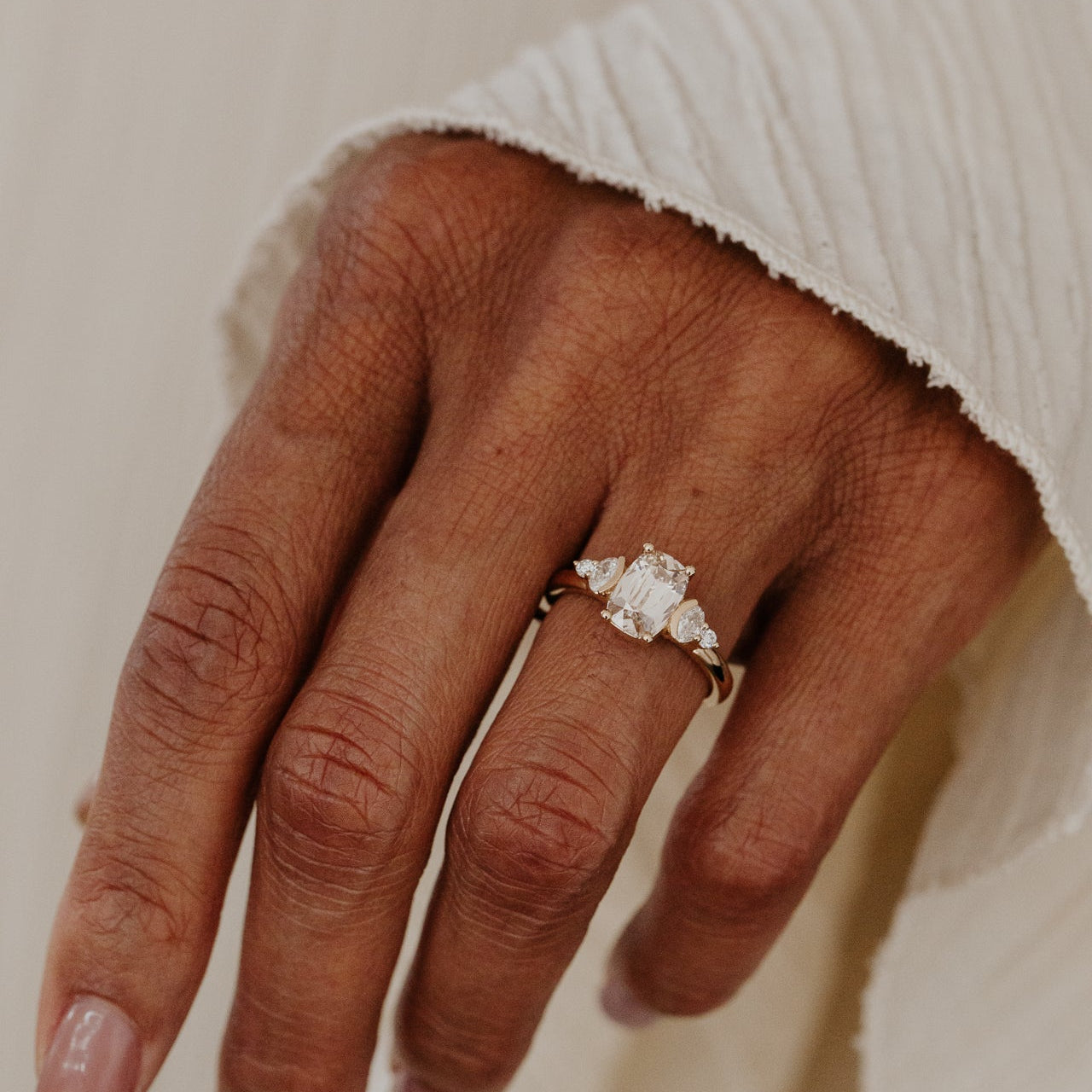 Hand wearing a champagne diamond ring on a neutral background.