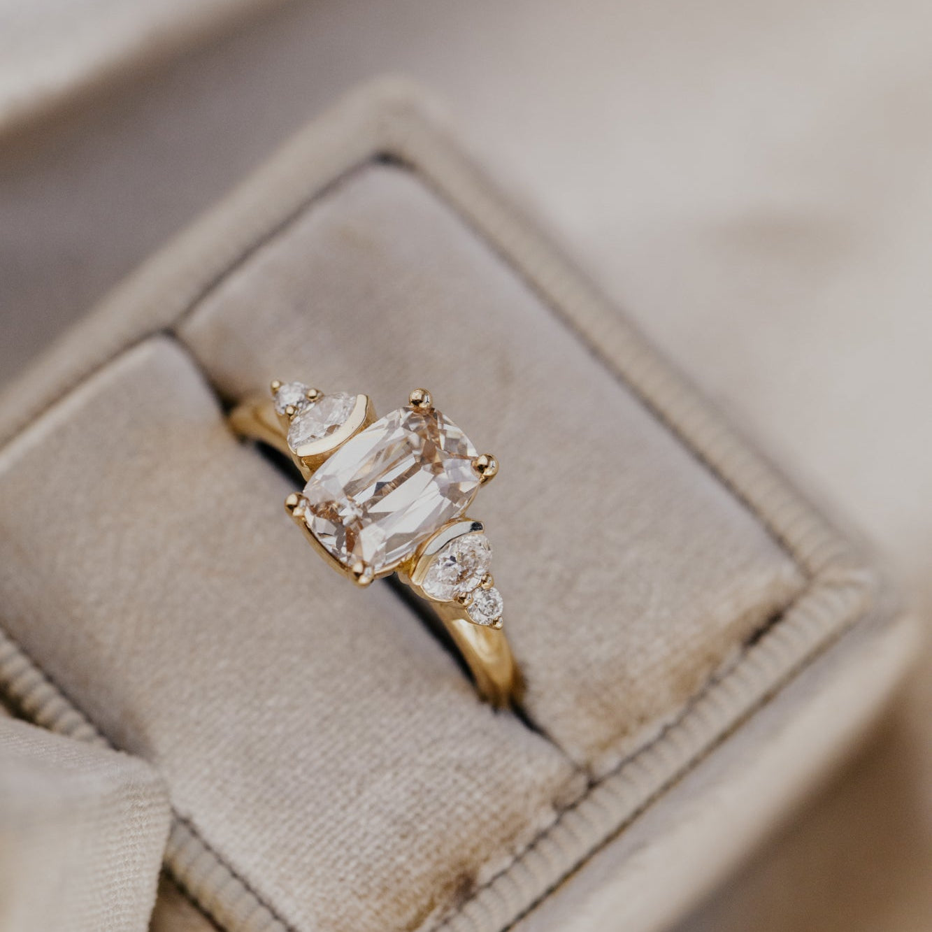 Gold engagement ring with a champagne diamond center stone on a textured beige surface.