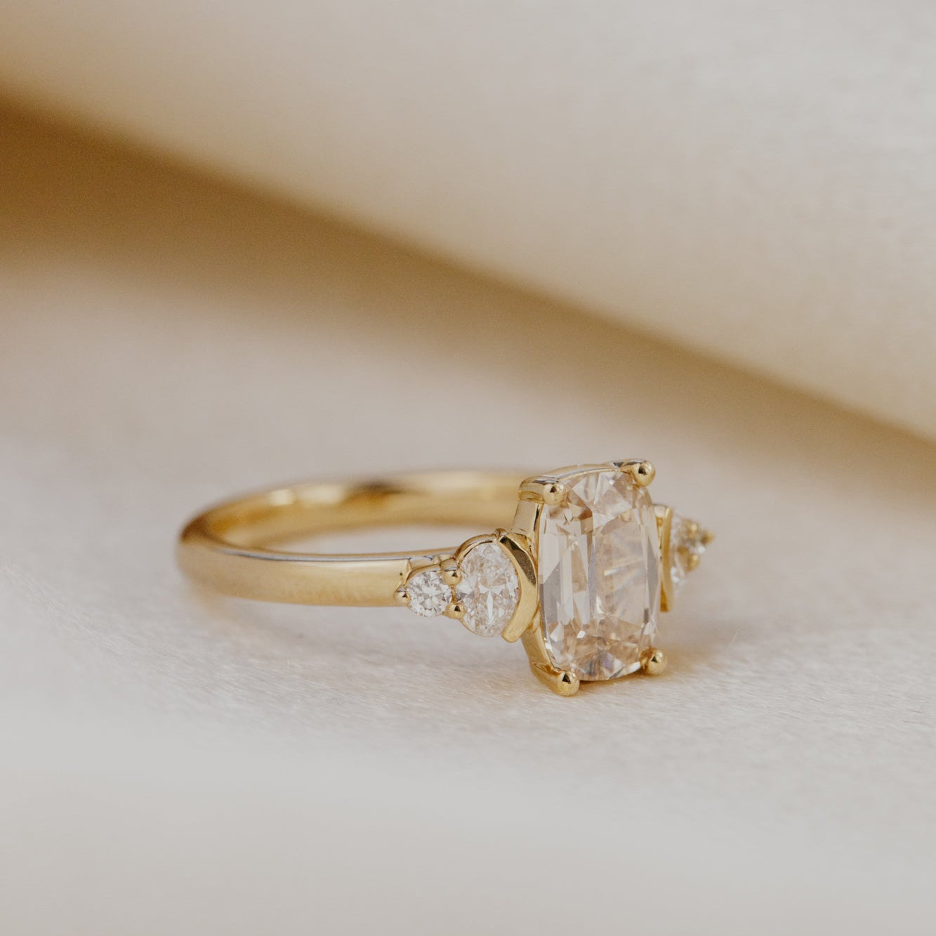Gold engagement ring with a champagne diamond on a soft beige background.