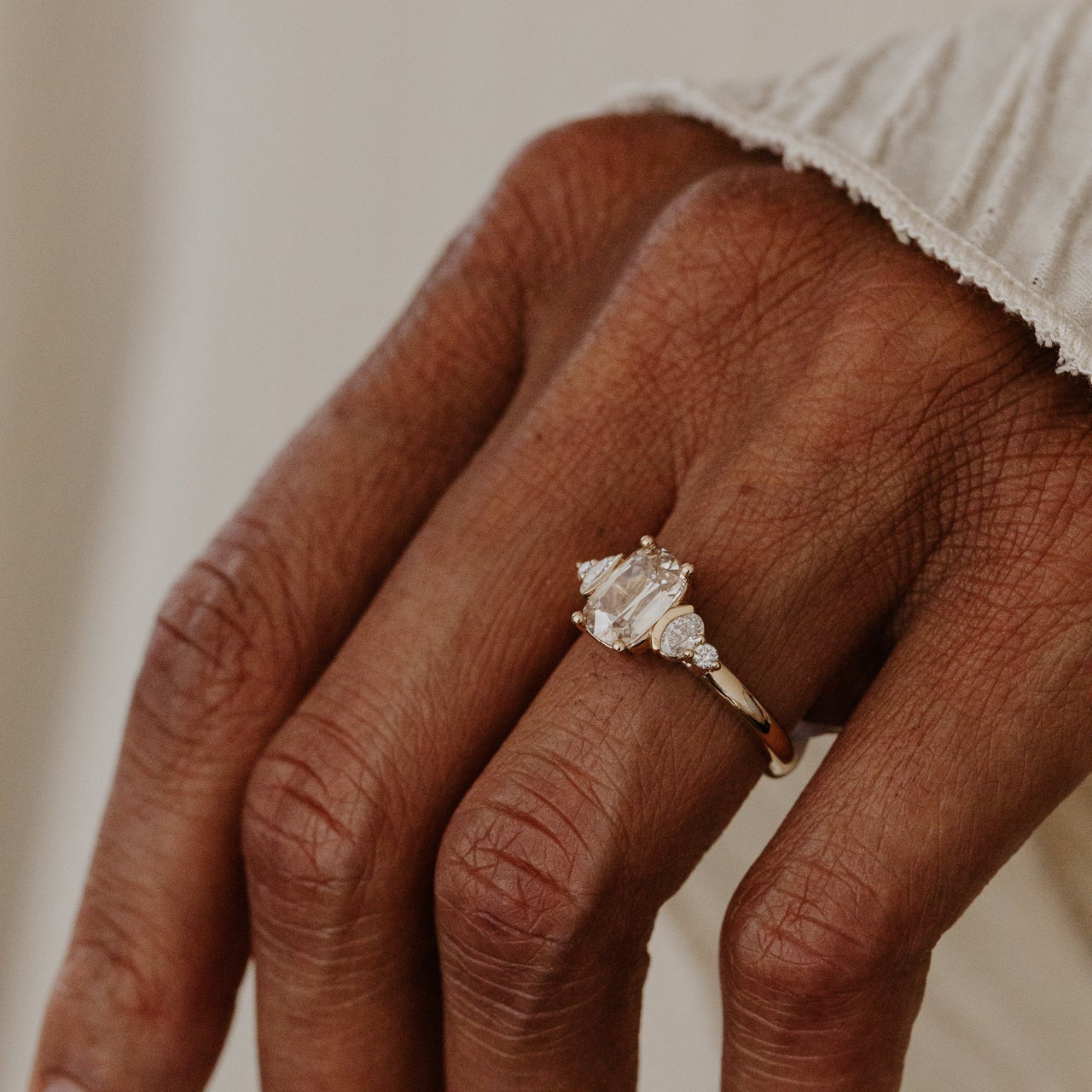 Close-up of a hand wearing a champagne diamond ring on a neutral background.