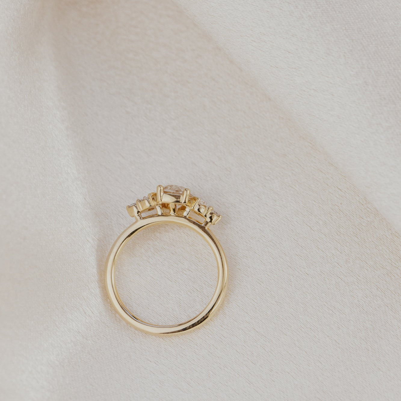 Gold engagement ring with a champagne diamond accents on a light beige background.