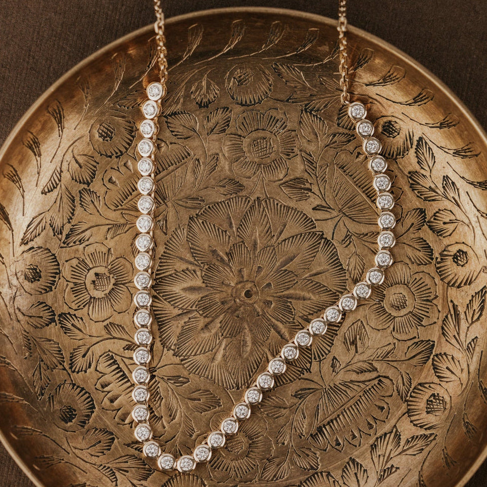 Diamond tennis necklace on a decorative bronze plate with floral patterns.