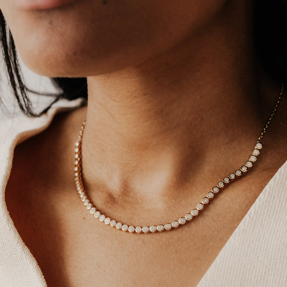 Close-up of a person wearing a delicate diamond tennis necklace.