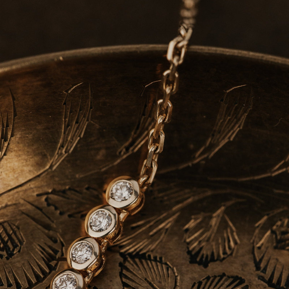 Gold tennis necklace with diamonds on a textured bronze surface.