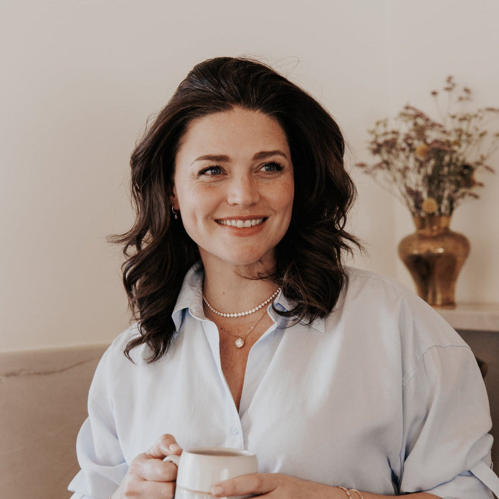 Woman holding a mug with a neutral background wearing a diamond tennis necklace.