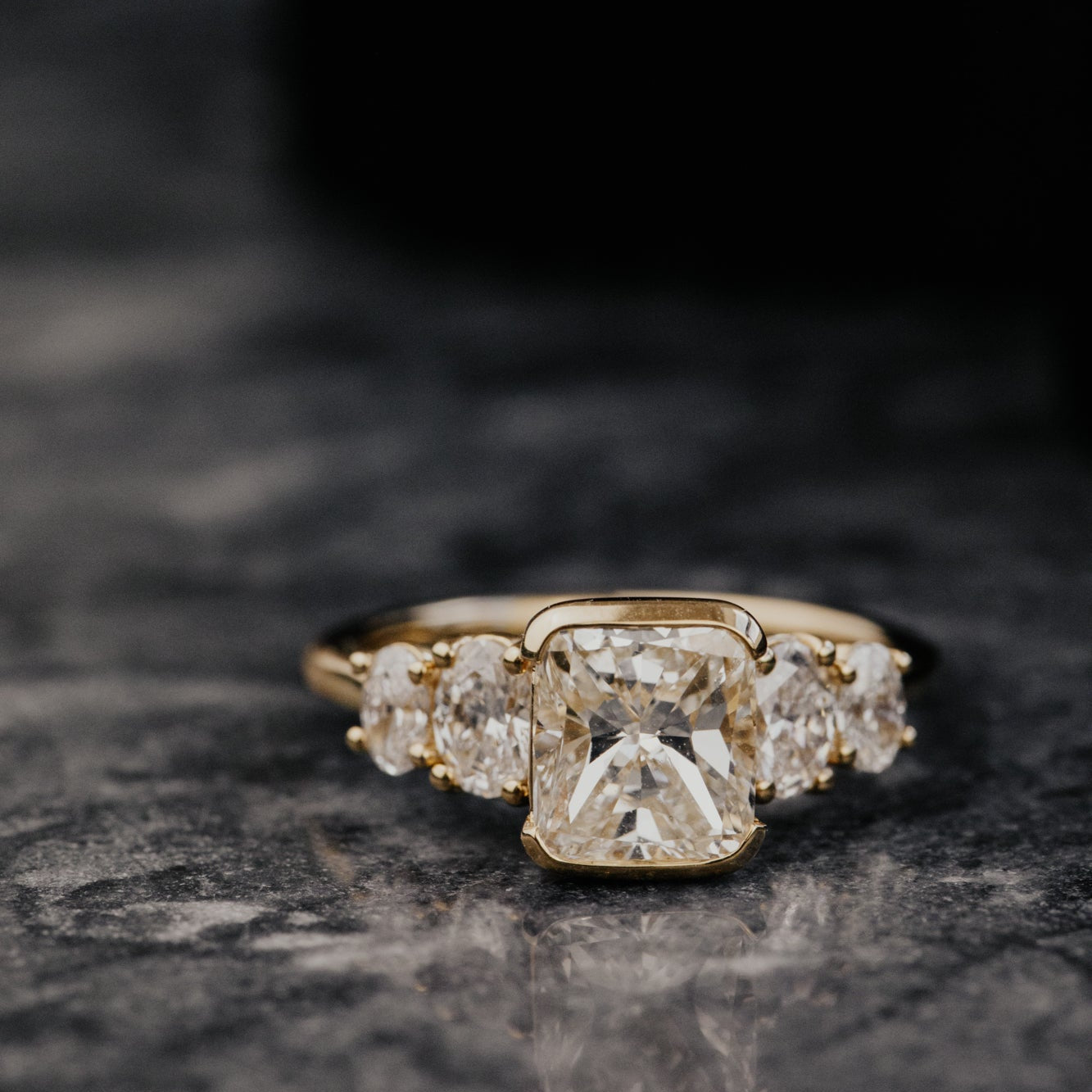 Cushion diamond ring on a dark textured surface.