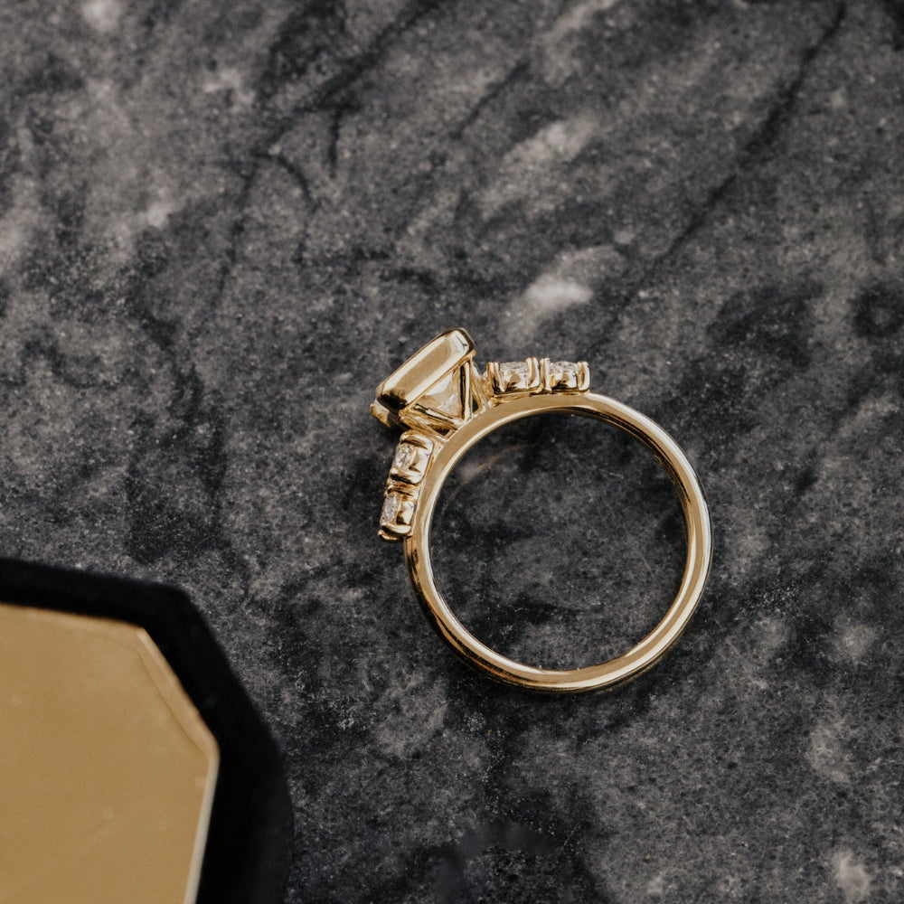 Gold ring with a cushion diamond on a dark marble surface.