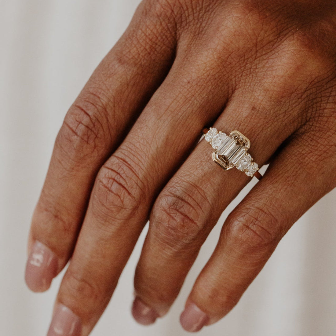 Hand wearing a emerald cut champagne diamond ring on a neutral background.