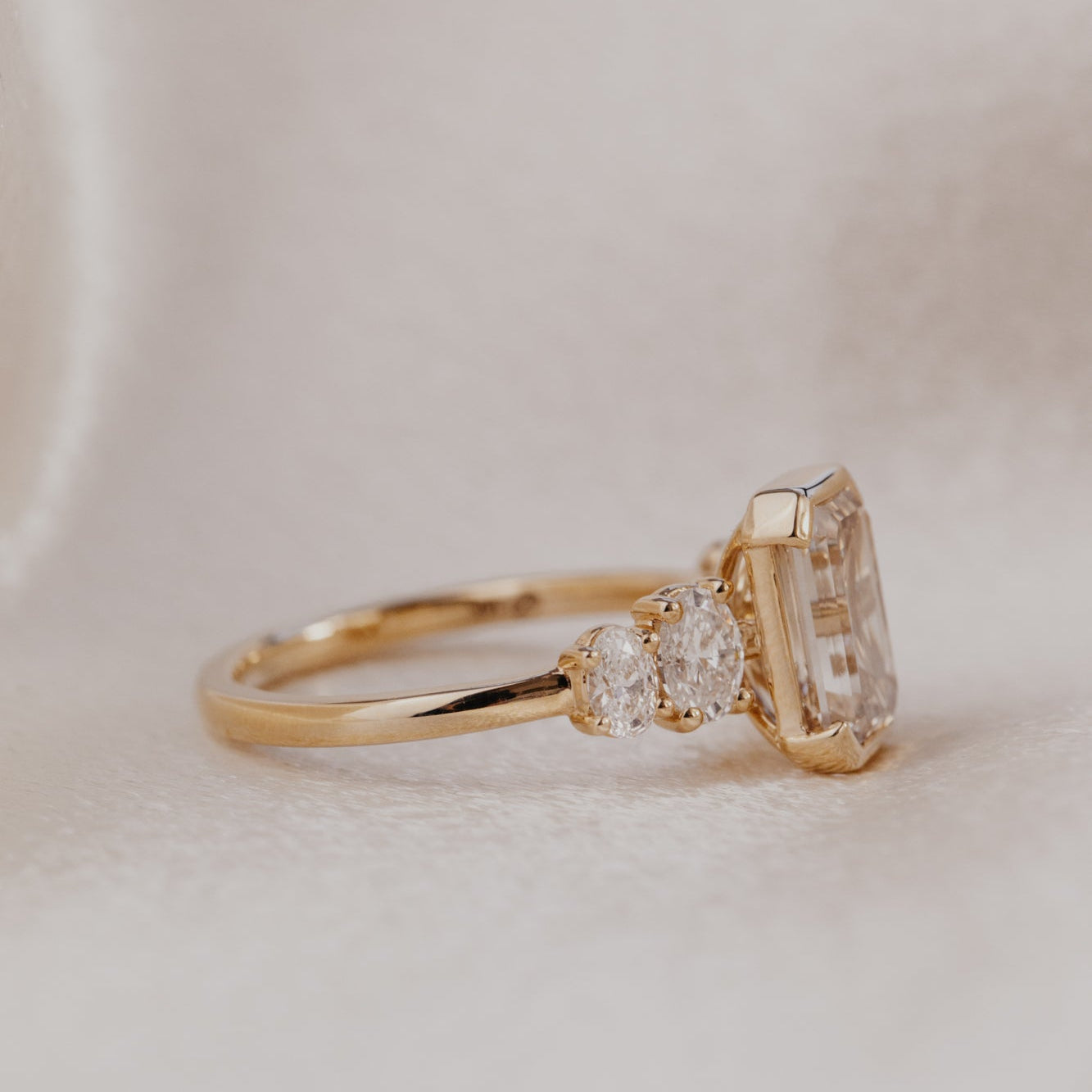 Gold ring with a emerald cut champagne diamond on a light background.