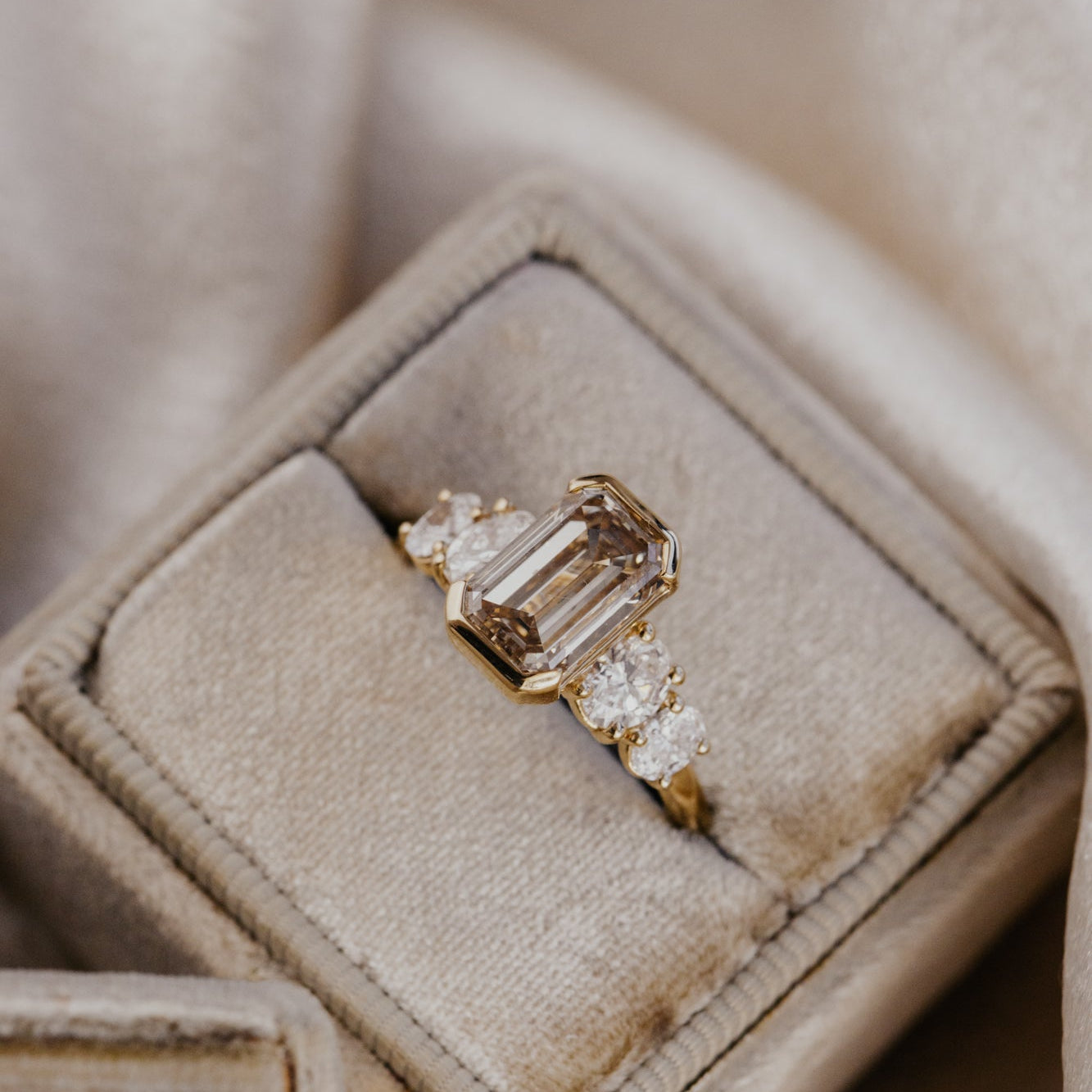 Emerald cut champagne diamond ring in a beige jewelry box on a soft beige background.
