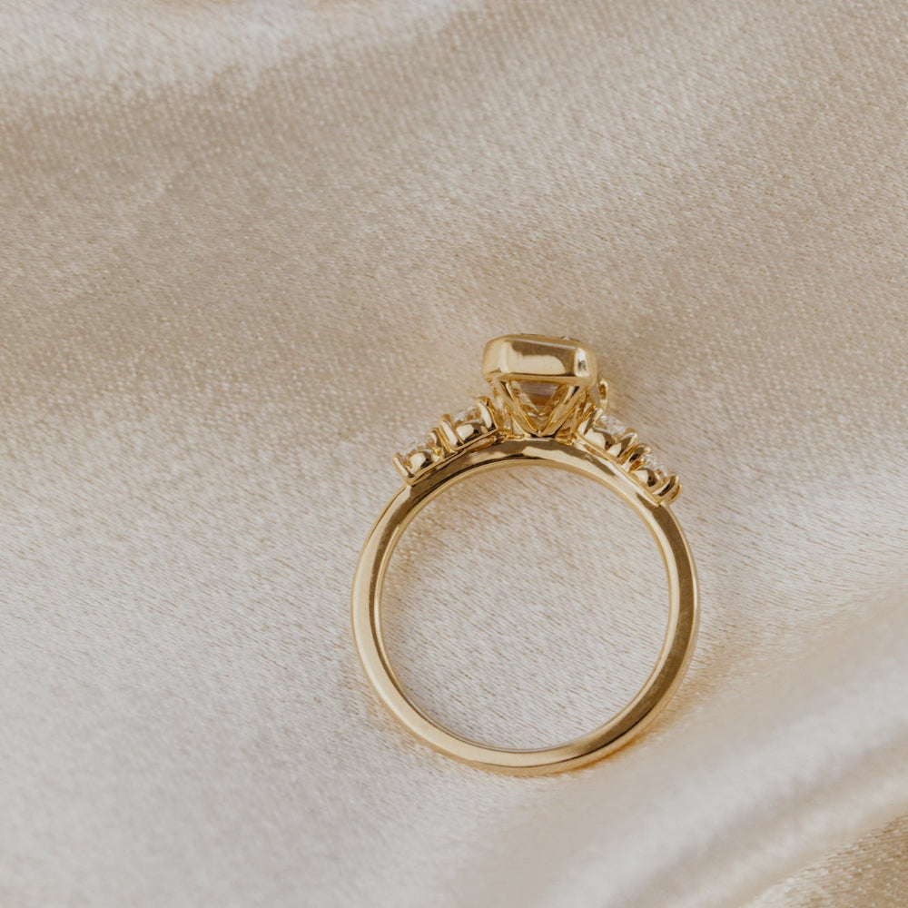 Gold ring with a emerald cut champagne diamond on a beige fabric background.