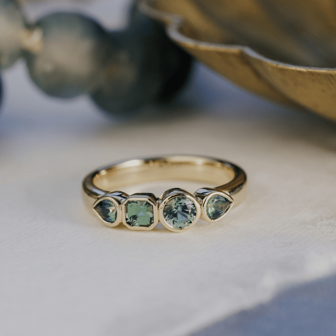 A 14k gold ring featuring four blue sapphire gemstones, displayed on a textured white surface with a soft background.