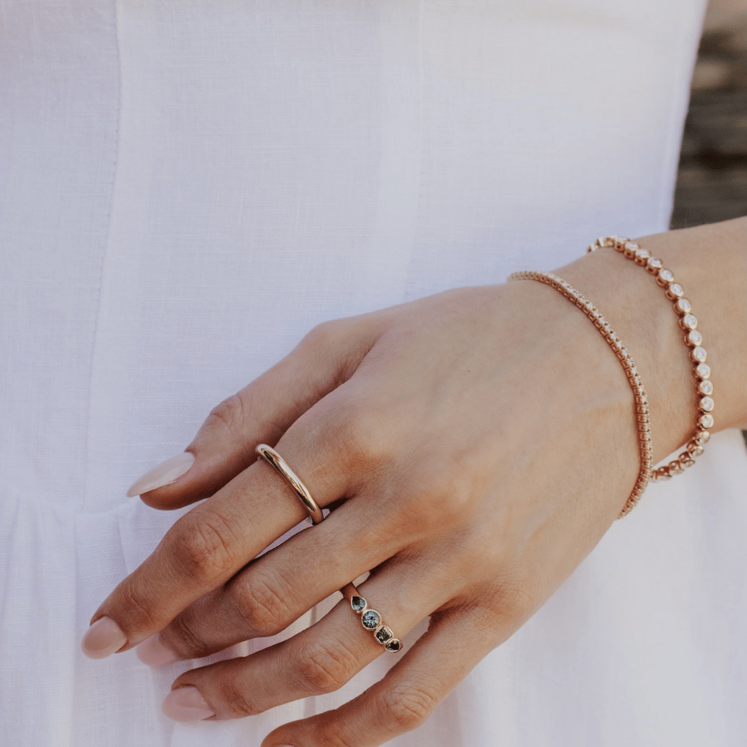 A 14k gold ring featuring four blue sapphire gemstones, displayed on the ring finger of a hand model in front of a white background.  