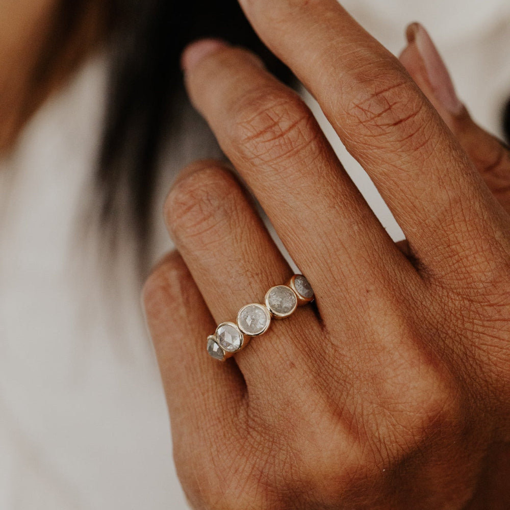 Close-up of a hand wearing the Blaine round ring with five rustic diamonds on a neutral background.