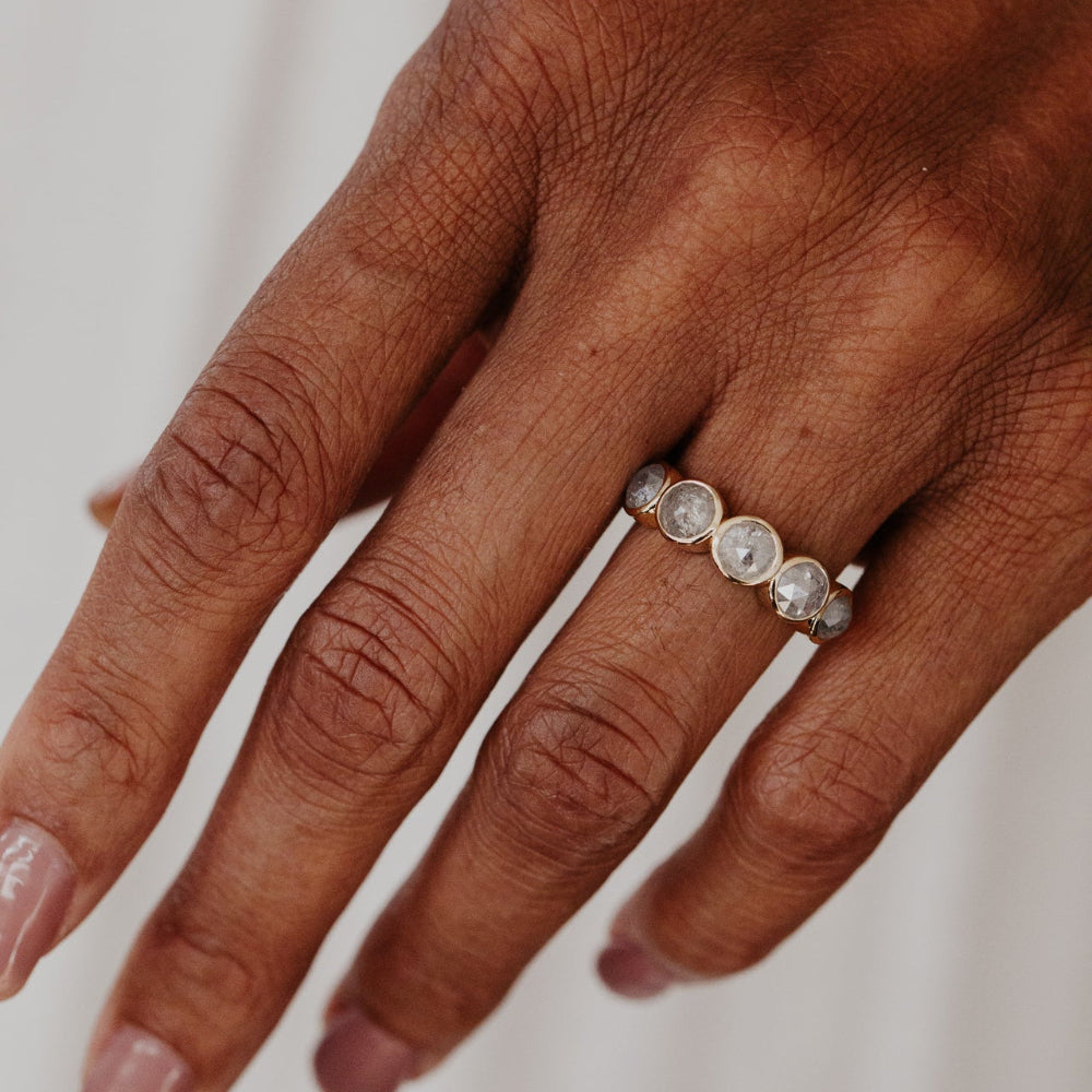 Hand wearing a Blaine gold ring with five round bezel-set rustic diamonds on a neutral background.