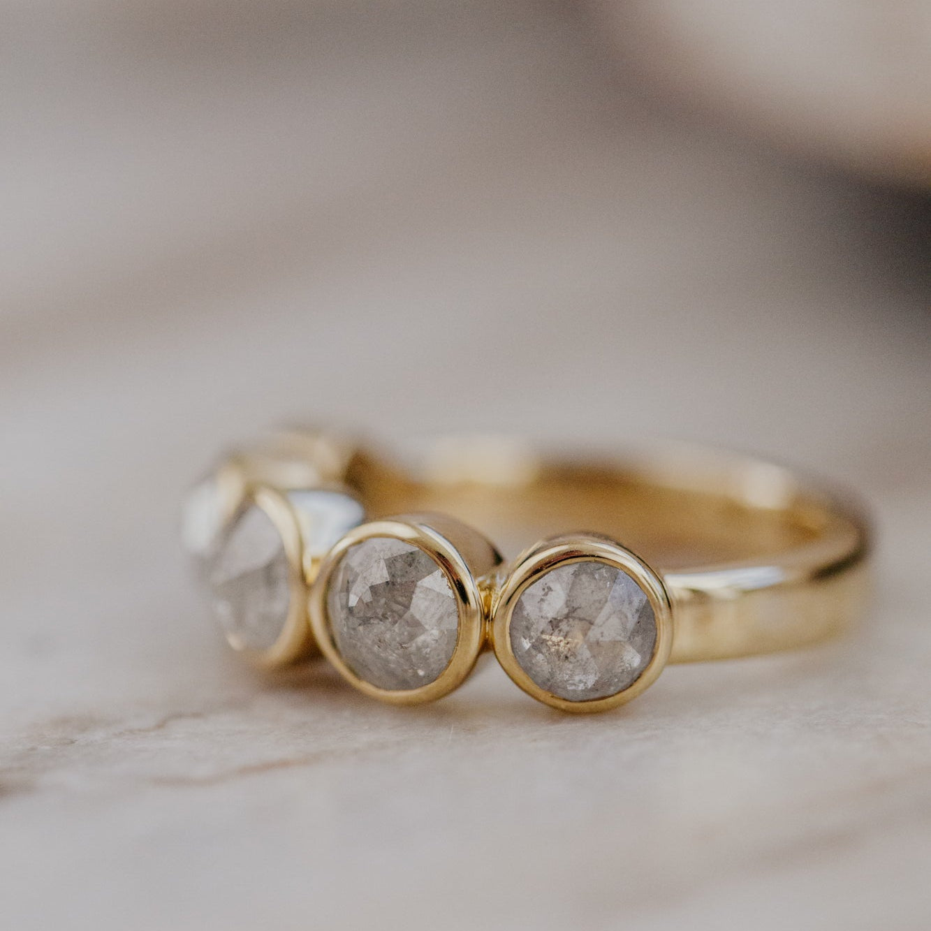 Gold Blaine ring with round rustic diamonds on a marble surface.