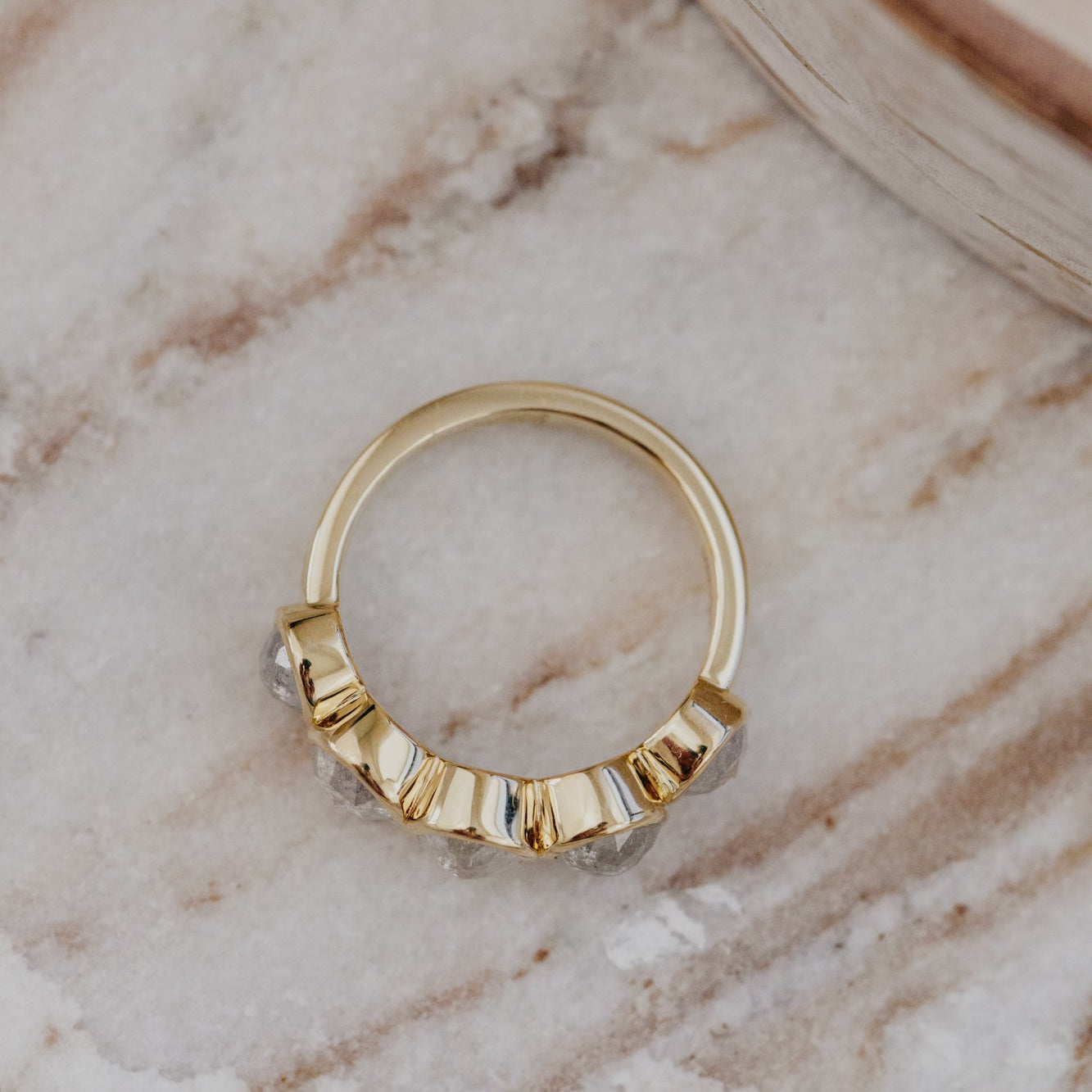 Gold Blaine ring with rustic diamonds in a bezel design on a marble surface.