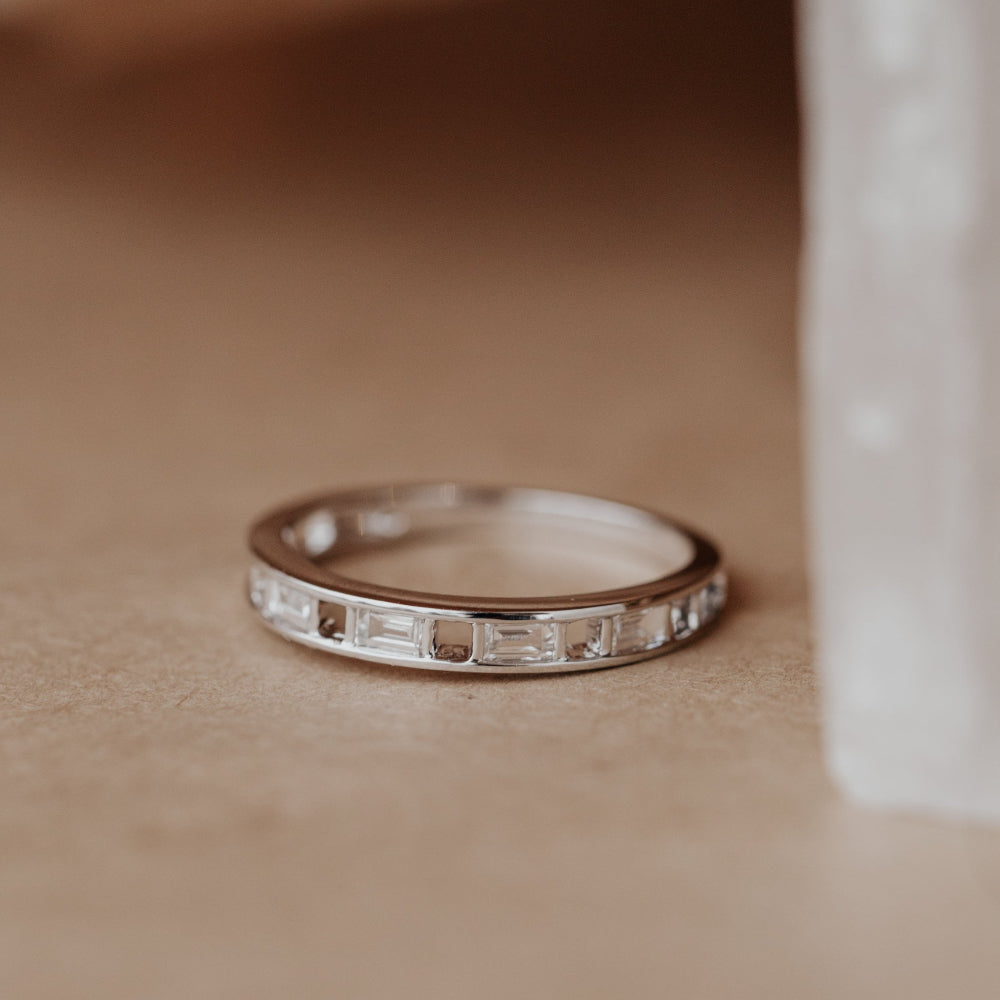 White gold Bridget wedding band with baguette diamonds on a textured surface.