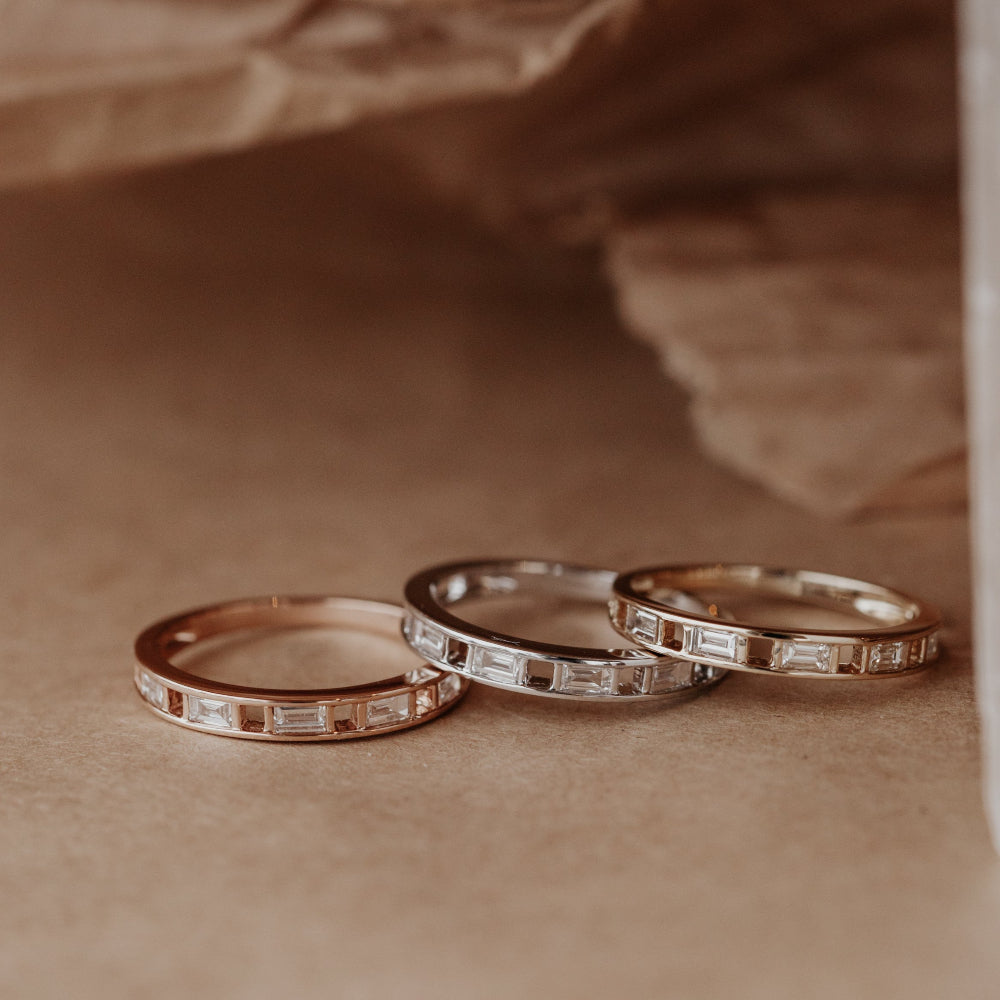 Three gold wedding bands with baguette diamond accents on a brown surface.