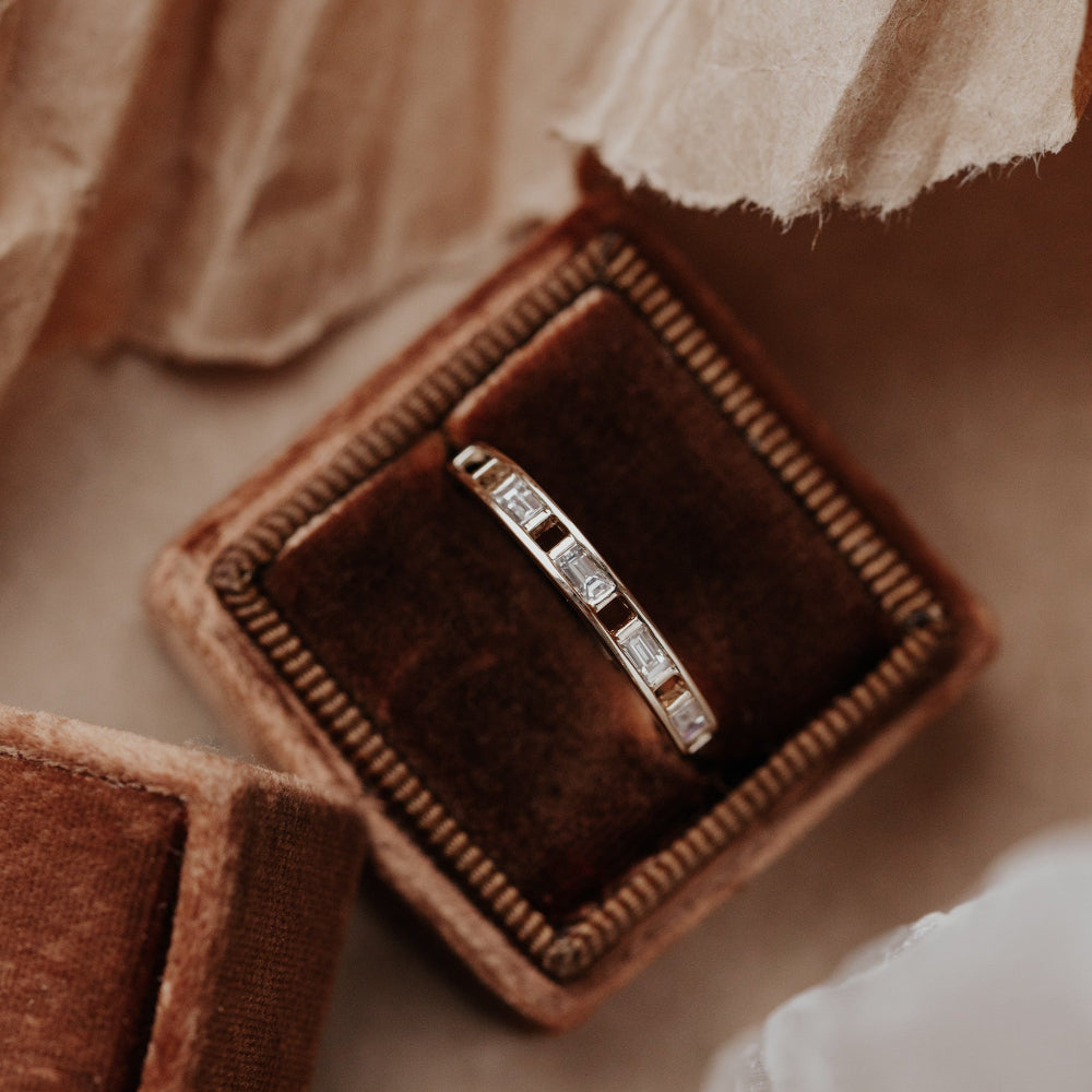 Diamond wedding band in a brown velvet box on a soft fabric background.