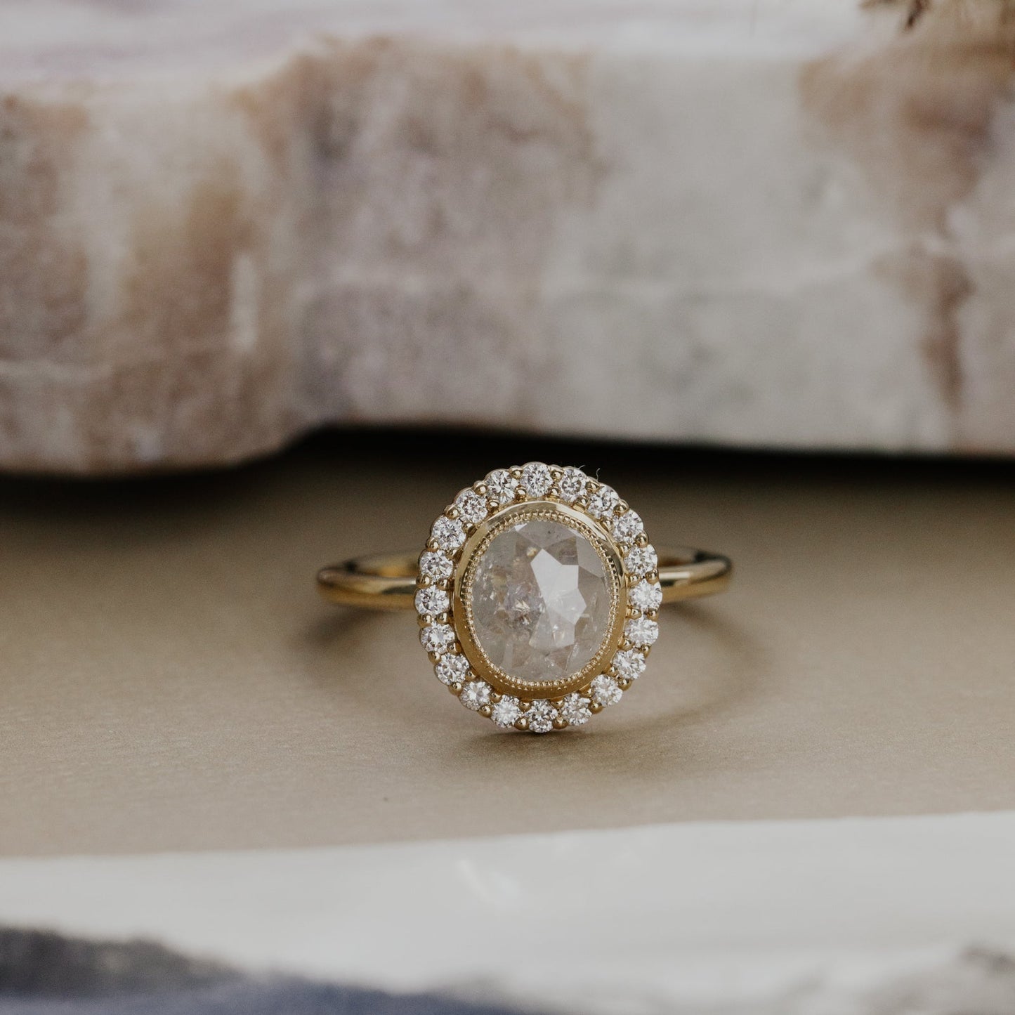 Gold ring with a large oval rustic diamond and a diamond halo on a textured surface.