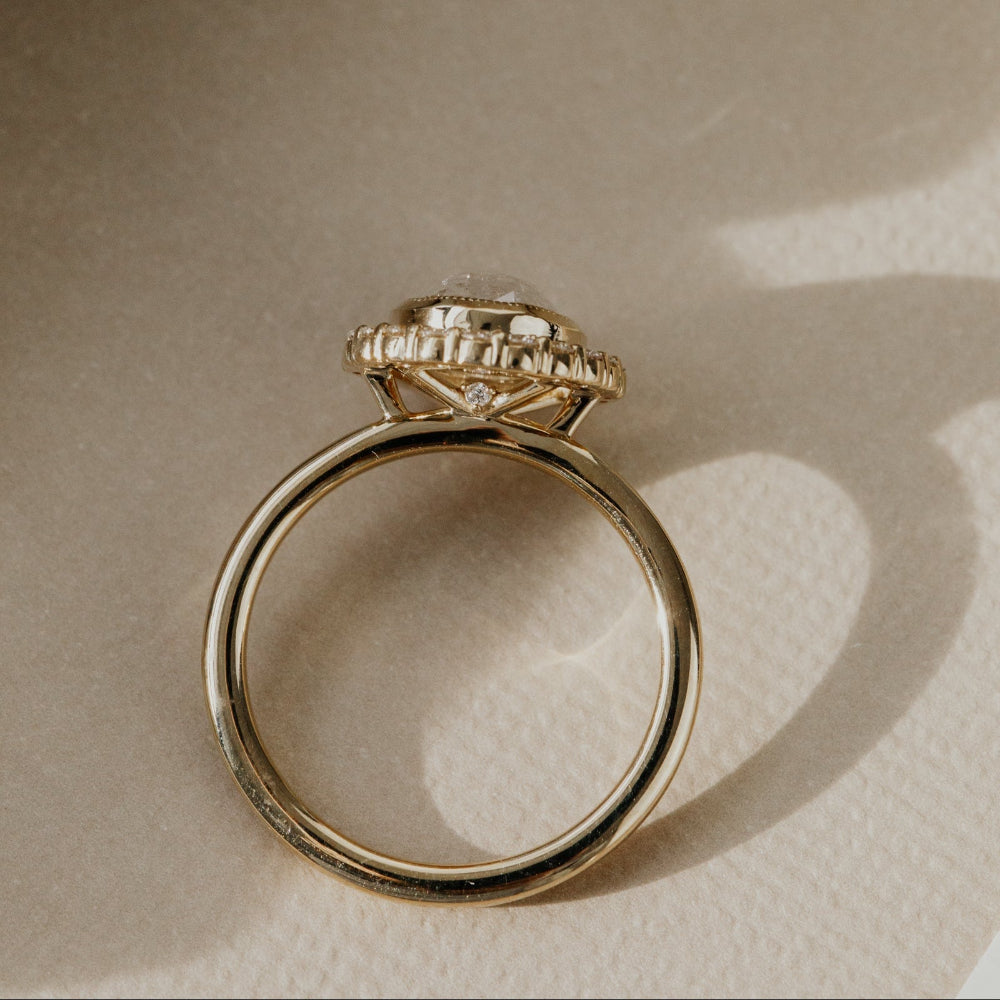 Gold ring with diamond accents on a beige background.