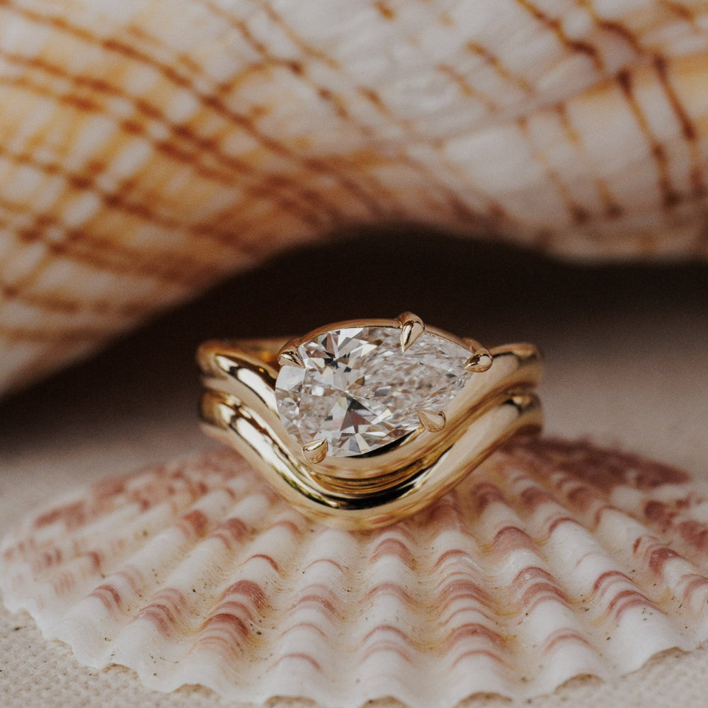 The Capri Pear Ring in 14k yellow gold featuring a lab-grown pear diamond prong set on a double wavy band, displayed inside a seashell. This 14k gold ring features a pear diamond center stone set in prongs on a double wavy band. This ring is made-to-order based on the selected customizations.