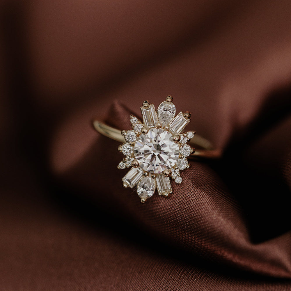 Gold engagement ring with a round diamond center stone and a diamond halo set on a brown silk fabric