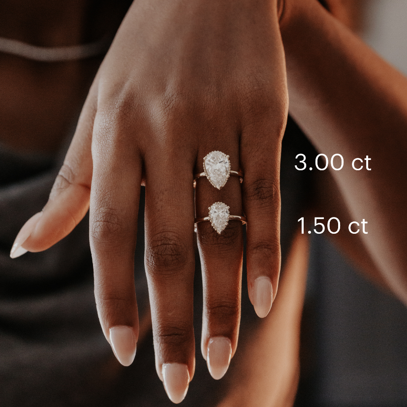 Hand wearing two Charlotte pear-shaped diamond rings with visible carat weights on a blurred background