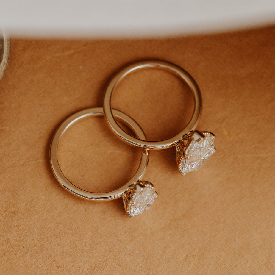 Two gold Charlotte engagement rings with pear-shaped diamond center stones on a brown surface.