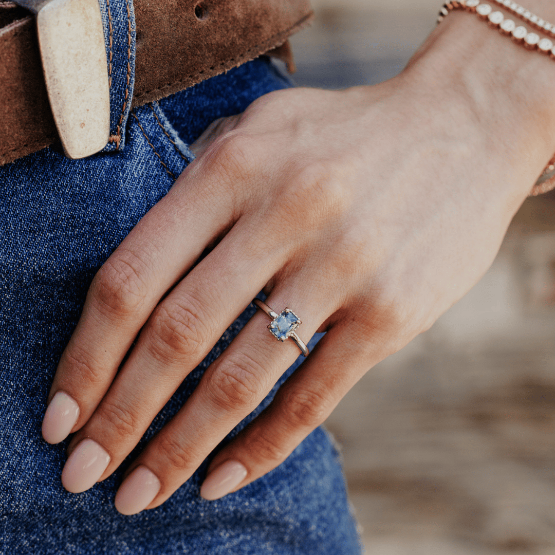 A 14k white gold ring featuring a dark blue sapphire gemstone, displayed on the ring finger of a hand model. 