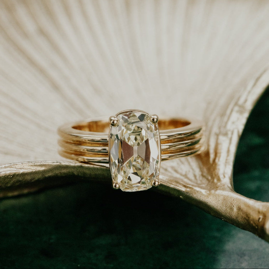 Gold ring with a large elongated cushion diamond on a textured surface.
