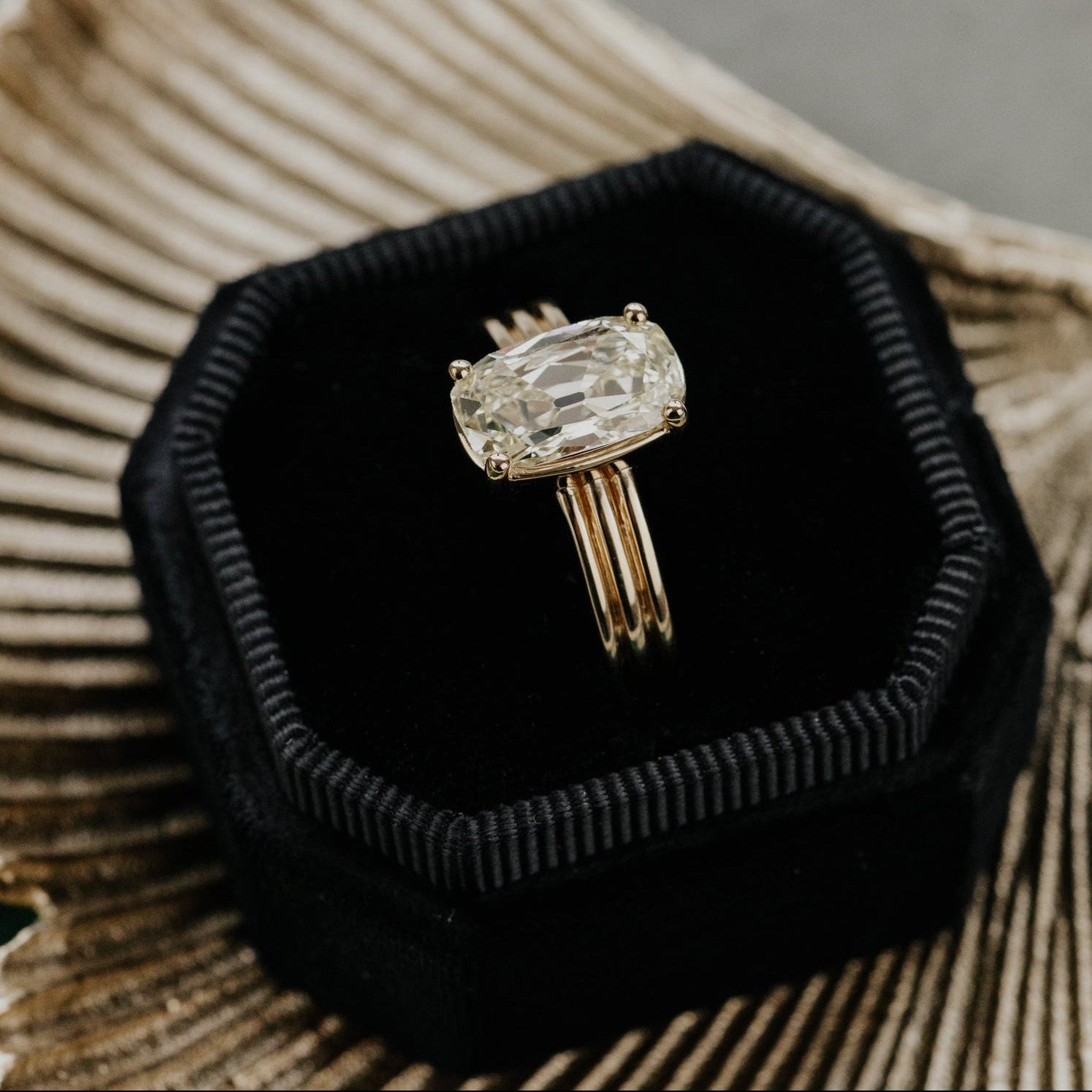 Gold ring with a large elongated cushion diamond in a black velvet box on a textured surface.
