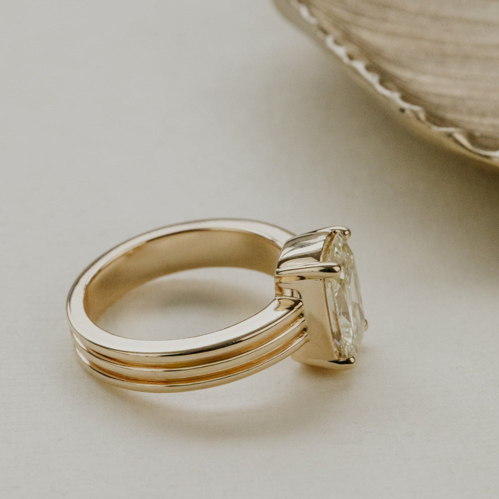 Gold ring with a elongated cushion diamond on a light background.