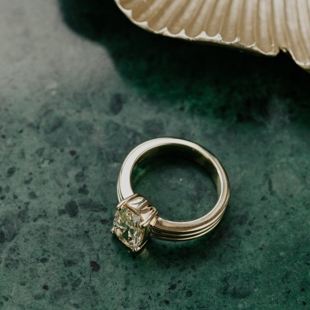Gold ring with a diamond on a textured green surface.