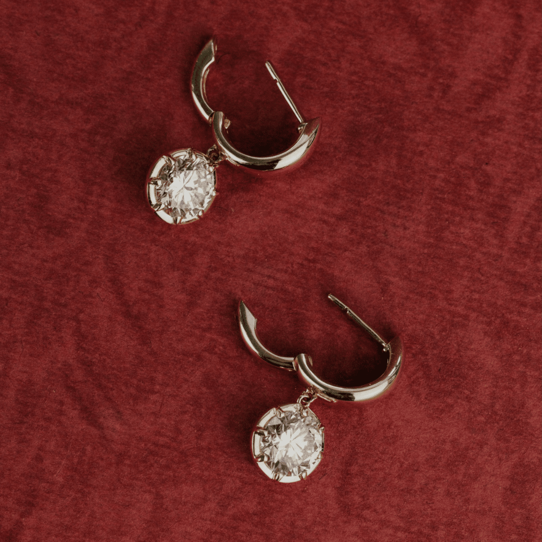 14k gold round cut, lab grown diamond dangle hoop earrings showcased on a textured red surface. 