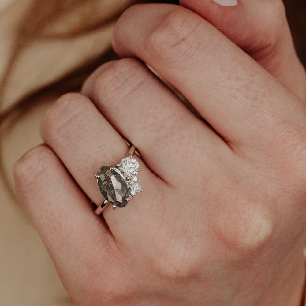 Close-up of a hand wearing an elegant ring with a galaxy diamond on a blurred background.