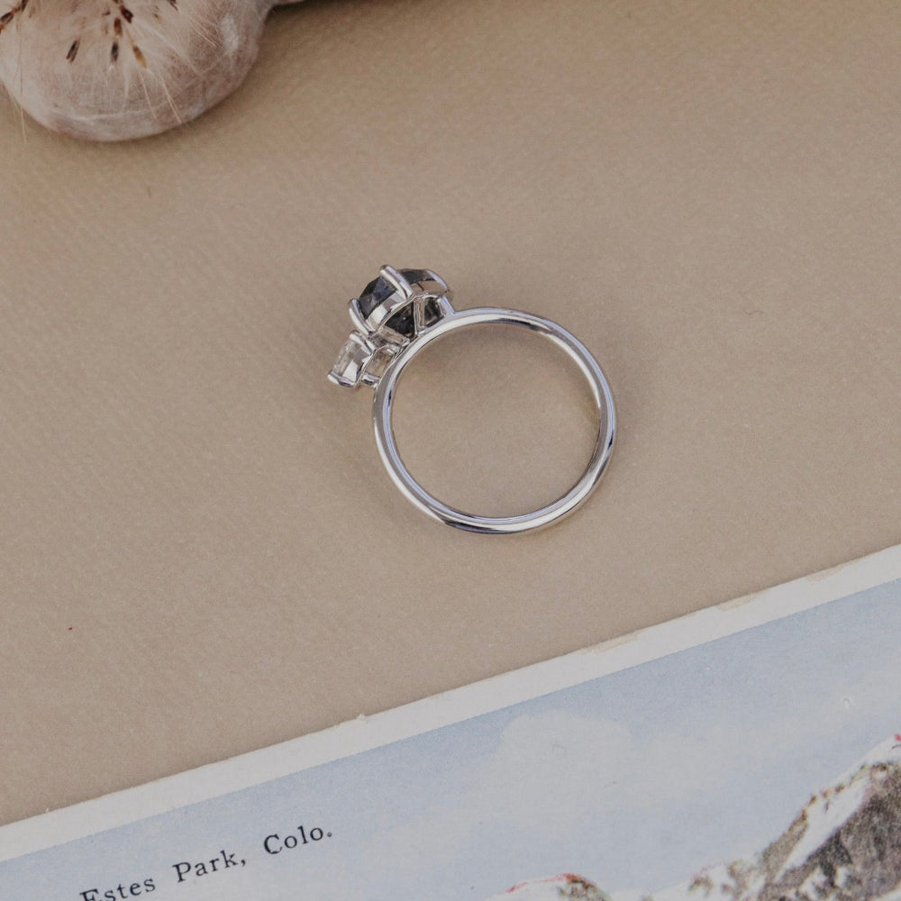 White gold ring on a textured surface with a scenic postcard underneath.