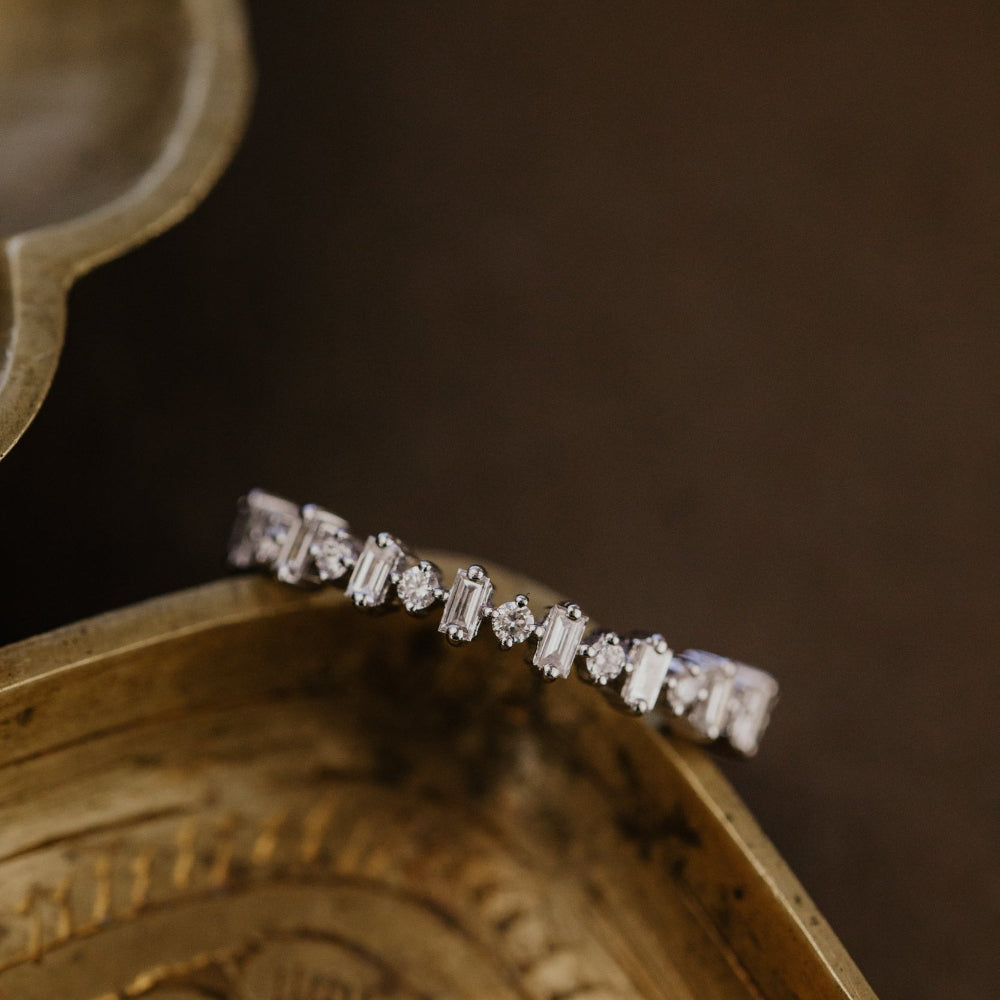 Diamond wedding band on an ornate gold dish with a dark background.