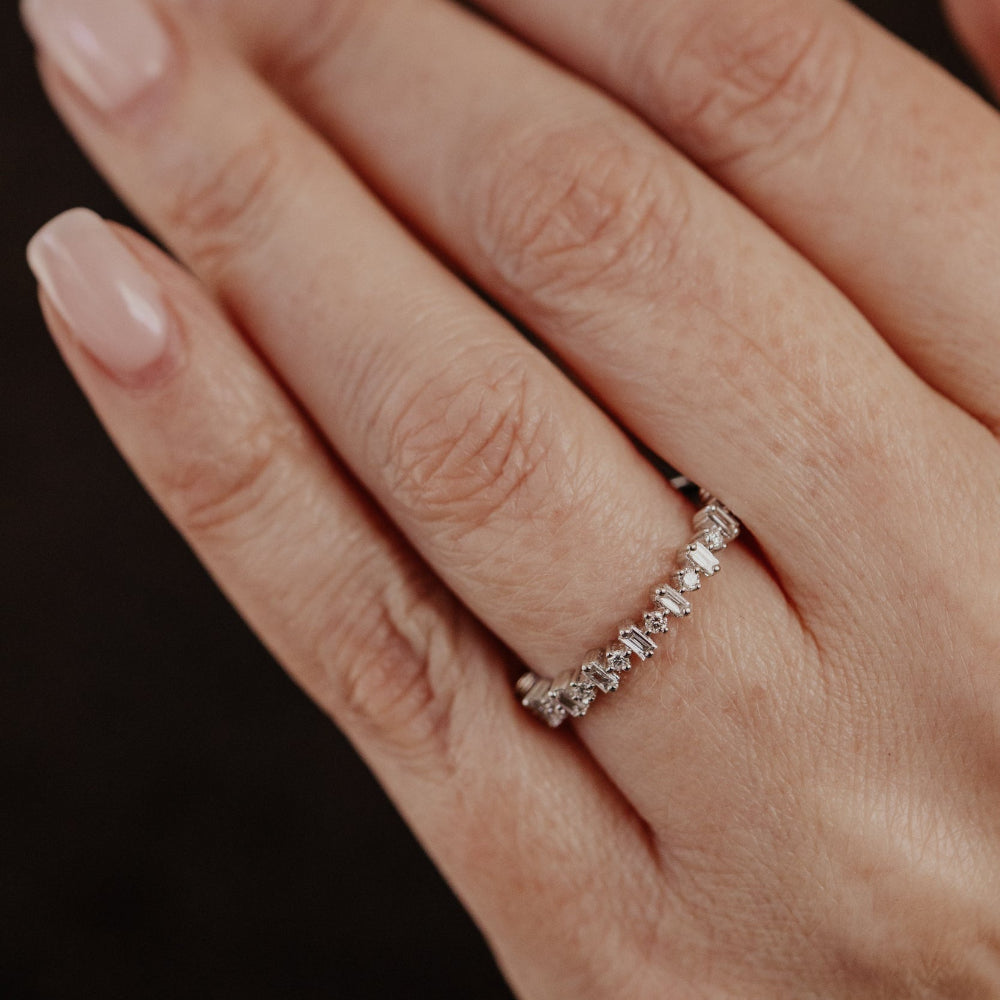 Close-up of a hand wearing a diamond wedding band on a dark background.