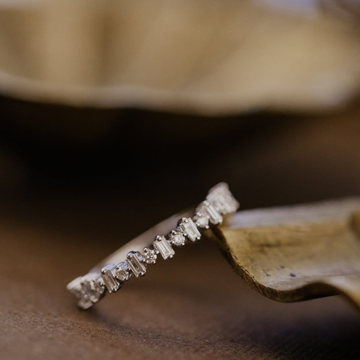 Close-up of a diamond wedding band on a wooden surface with a blurred background.