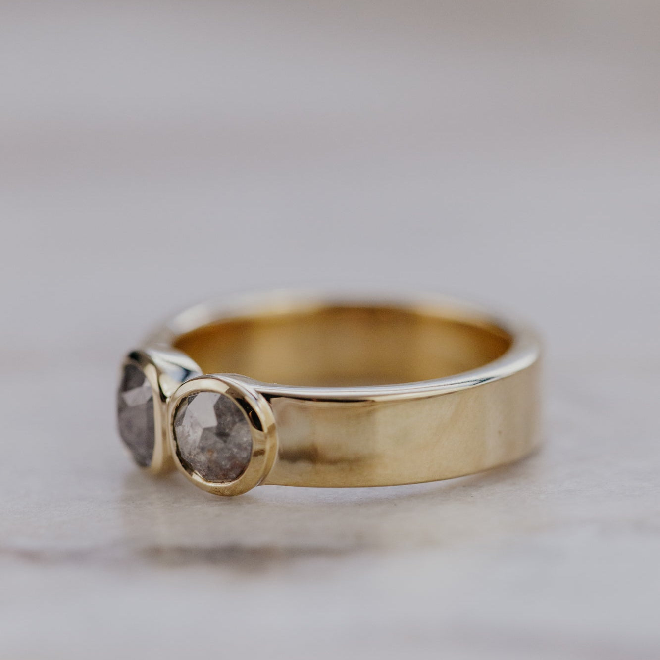 Gold ring with two small rustic diamond stones on a blurred background.