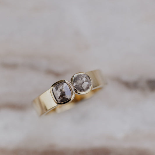 Gold ring with two rustic diamond gemstones on a marble background.
