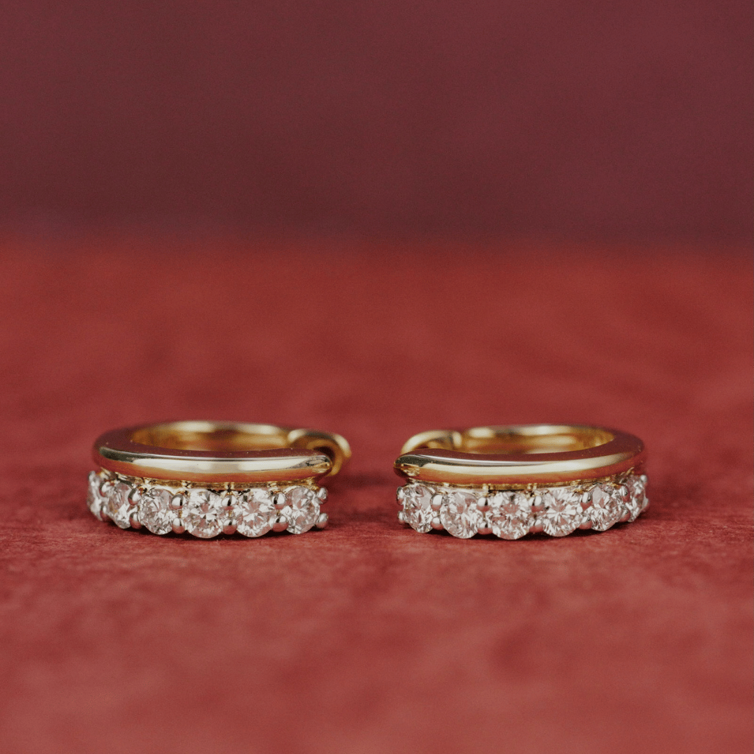 14k gold diamond huggie and plain huggie earrings showcased on a textured red surface. 