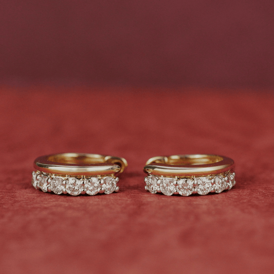 14k gold diamond huggie and plain huggie earrings showcased on a textured red surface. 